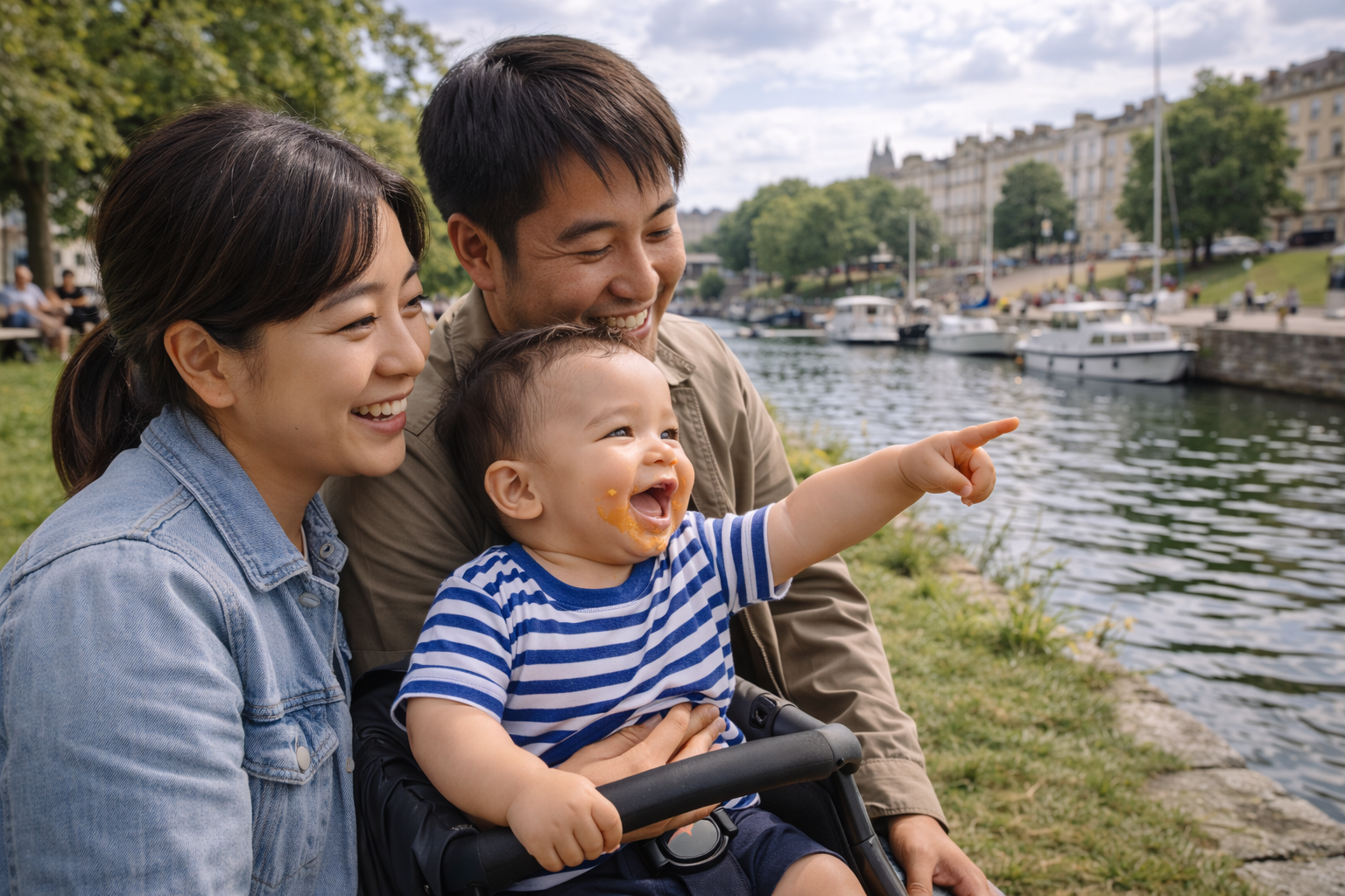 A family with a baby at a riverside setting in a UK city, boats visible, green space nearby, baby pointing at something with interest
